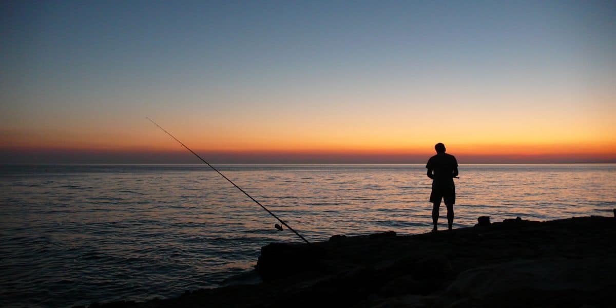 An angler fishing from rocks at sunset