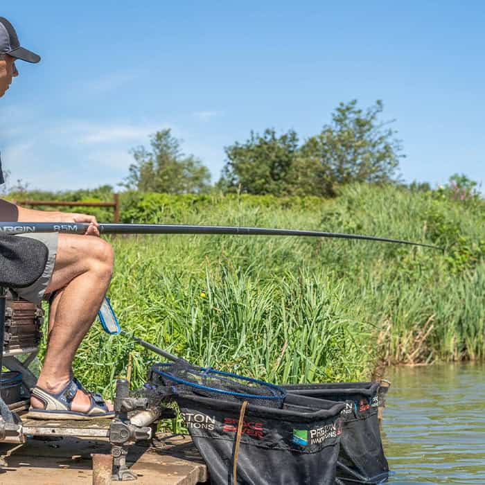 An angler on a box fishing a short 8.5m margin pole tight to the near bank with keepnets in the water
