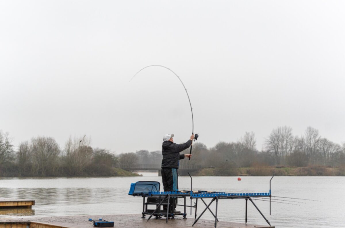 Angler casting a distance feeder rod loaded into a deep curve over open water